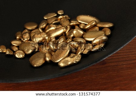 Gold pan with golden nuggets inside on wooden background