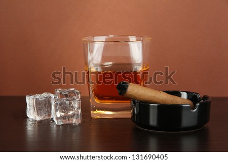 Glass of whiskey and cigar on brown background