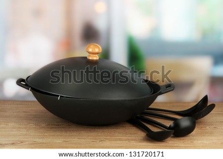 Black wok pan and spoons on kitchen table, close up
