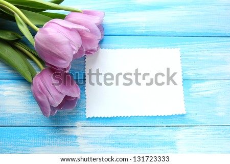 Beautiful bouquet of purple tulips and blank card on blue wooden background