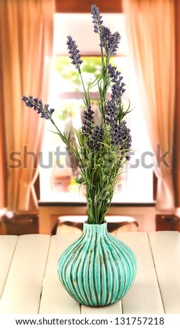 Decorative ceramic vase with lavender on wooden table on window background