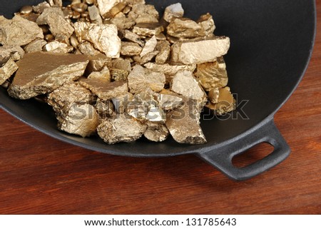 Gold pan with golden nuggets inside on wooden background
