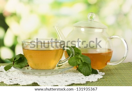 Cup of tea with mint on table on bright bacground