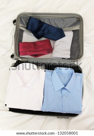 Open grey suitcase with clothing on bed