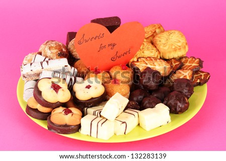Sweet cookies on plate with valentine card on pink background