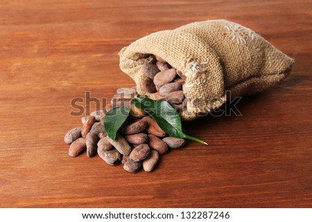 Cocoa beans in bag with leaves on wooden background