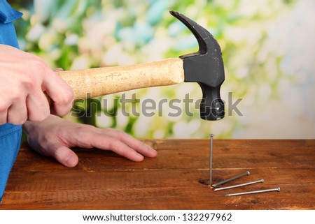 Builder hammering nails into board on natural background