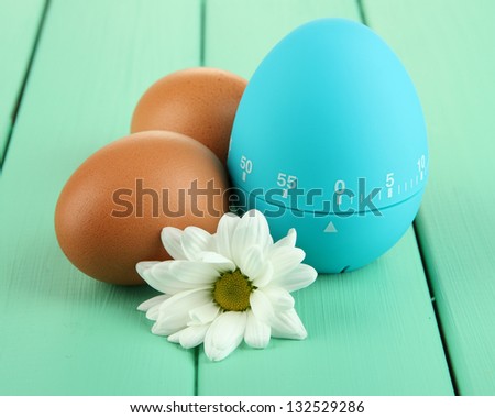Blue egg timer and eggs, on color  wooden background