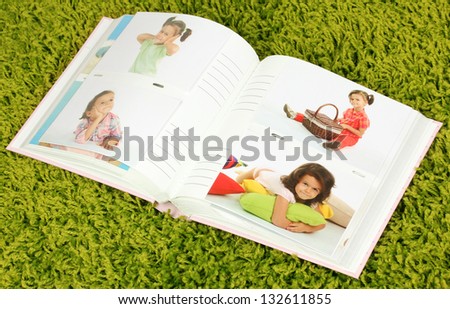 Open photo album with pictures on green carpet