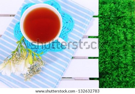 Beautiful composition with cup of tea and flowers on wooden picnic table close-up
