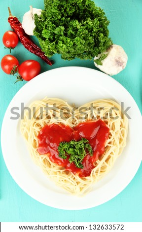 Cooked spaghetti carefully arranged in  heart shape and topped with tomato sauce, on  blue background