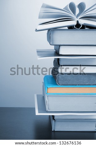 Stack of interesting books and magazines on wooden table on blue background