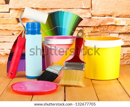 Paint pots, paintbrushes and coloured swatches on wooden table on stone wall background