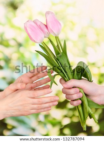 Mans hand giving woman\'s hand a flower bouquet with tulips, on green background
