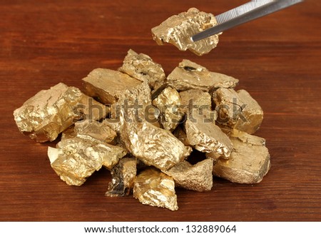 Tweezers holding golden nugget on wooden background
