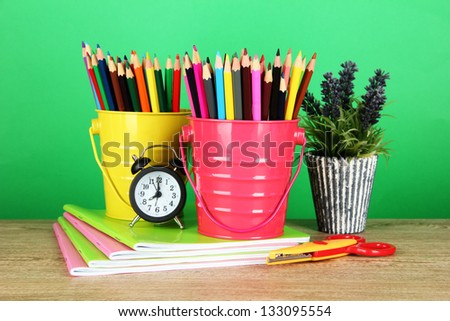 Colorful pencils with school supplies on table on green background