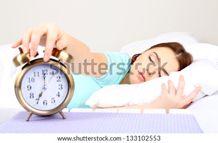Beautiful young woman sleeping on bed with alarm clock in bedroom