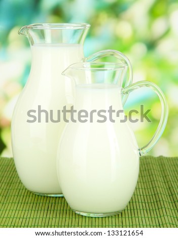 Pitchers of milk on table on bright background