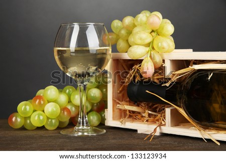 Wooden case with wine bottle, wineglass and grape on wooden table on grey background