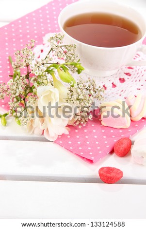 Beautiful composition with cup of tea and flowers on wooden picnic table close-up
