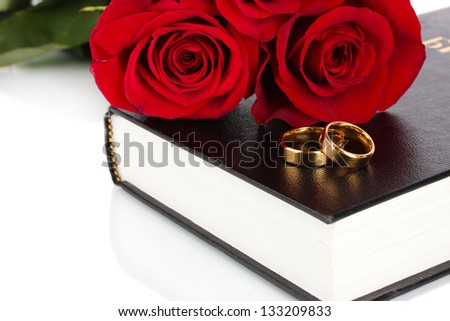 Wedding rings with roses on bible isolated on white