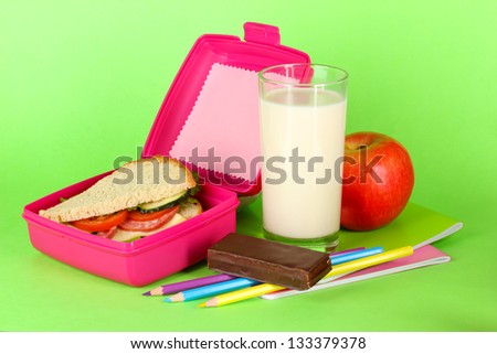 Lunch box with sandwich,apple,milk and stationery on green background