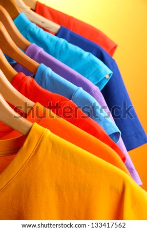 Lots of T-shirts on hangers on orange background