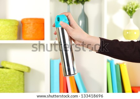 Sprayed air freshener in hand on white shelves background