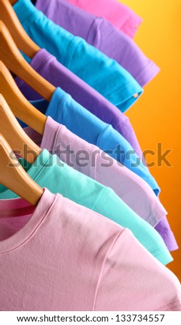 Lots of T-shirts on hangers on orange background