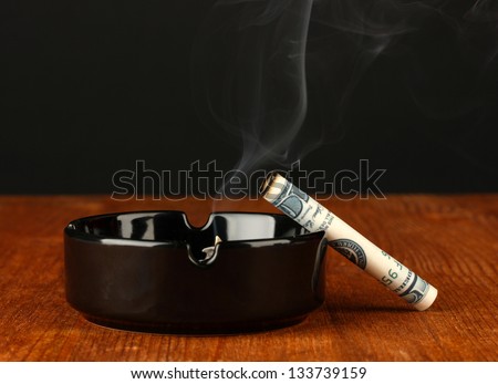 smoking cigarette of the 100 dollar bill and an ashtray on black background