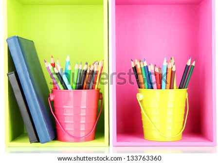 Colorful pencils in pails with writing-pad on shelves
