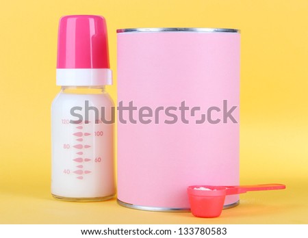 Powdered milk with baby bottle of milk on yellow background
