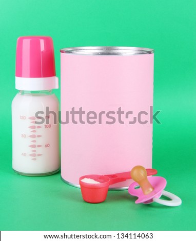 Powdered milk with baby bottle of milk and nipple on green background