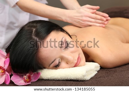 Beautiful young woman in spa salon getting massage with spa stones, on dark background