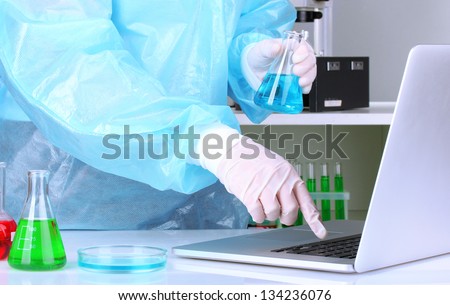 Scientist entering data on laptop computer with test tube close up