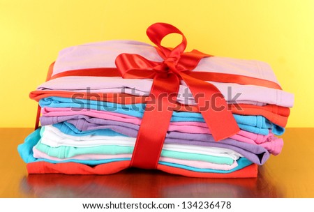 Pile of clothing with red ribbon and bow on table on yellow background
