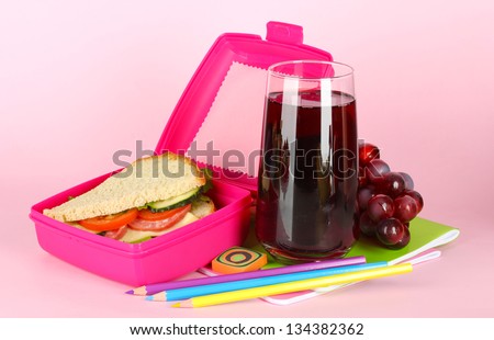 Lunch box with sandwich,grape,juice and stationery on pink background