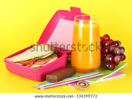 Lunch box with sandwich,grape,juice and stationery on yellow background
