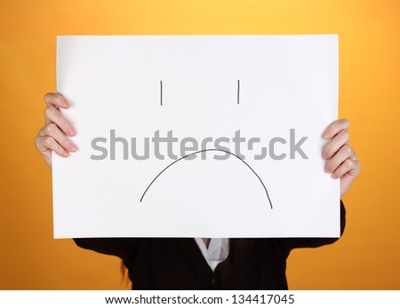 Woman holding paper with sad emoticon, on color background