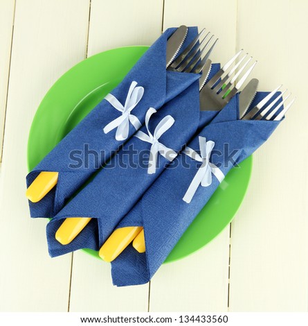 Forks and knives wrapped in blue paper napkins, on color wooden background