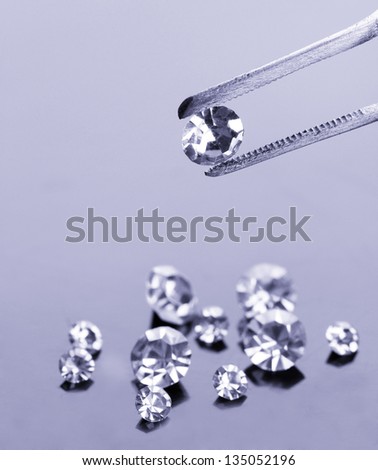 Beautiful shining crystal (diamond) in the tweezers, on grey background