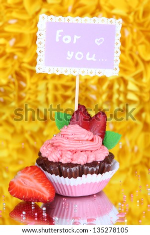 Beautiful strawberry cupcake with postcard on decorative yellow background