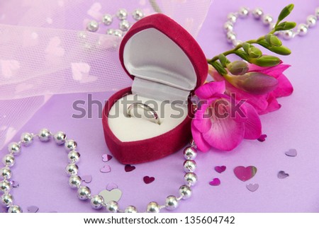 Beautiful box with wedding ring and flower on purple background