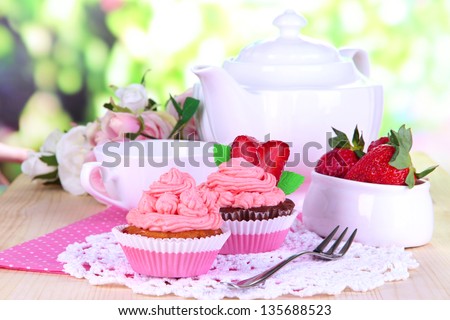 Beautiful strawberry cupcakes and flavored tea on dining table on natural background