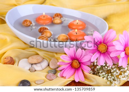 Beautiful candles swim in beautiful plate on yellow fabric close-up