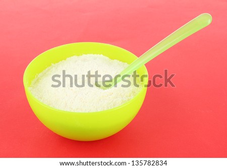 Powdered milk in bowl for baby and spoon on red background
