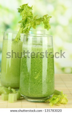Glasses of green celery juice on bamboo mat, on green background