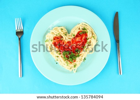 Cooked spaghetti carefully arranged in  heart shape and topped with tomato sauce, on color background