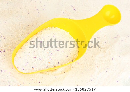 Washing powder in measuring cup on powder background