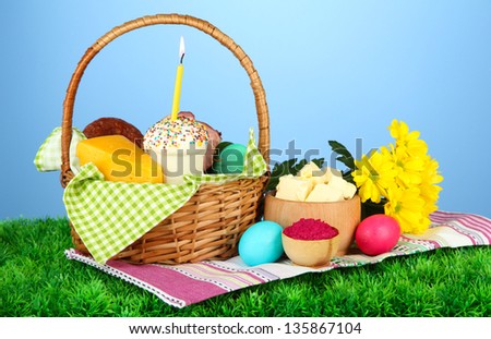 Easter basket: Conceptual photo of traditional easter food in wicker basket, on green grass, on color background